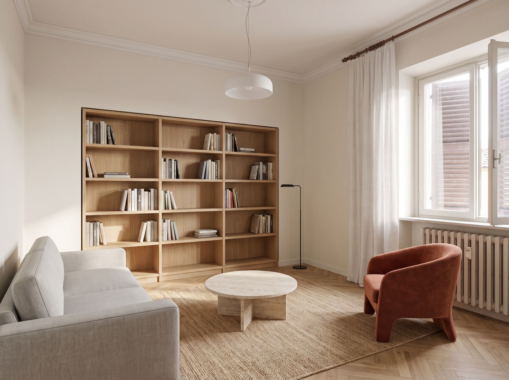Lo stesso soggiorno dopo i lavori: parquet a spina di pesce, pareti bianche, libreria in rovere libera, divano grigio contro la parete di sinistra, tavolino in travertino e poltrona rivolta al divano.